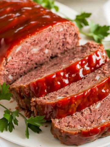 Chicken Meatloaf Recipe with a tender and juicy texture, sliced and served on a white plate. Topped with a rich, savory glaze and garnished with fresh parsley, this homemade meatloaf is a delicious comfort food dish.