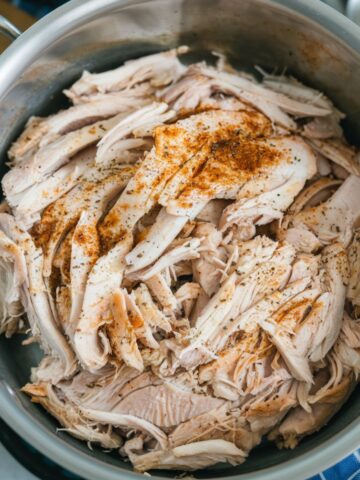 A pot filled with Instant Pot Shredded Chicken, seasoned with spices for extra flavor. This tender and juicy shredded chicken is perfect for meal prep, tacos, sandwiches, and salads. An easy, protein-packed recipe made in the Instant Pot.