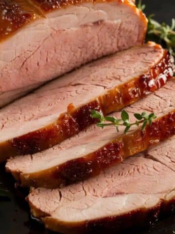 Sliced, juicy smoked pork loin with a caramelized glaze and fresh thyme garnish, highlighting a flavorful smoked pork loin recipe.