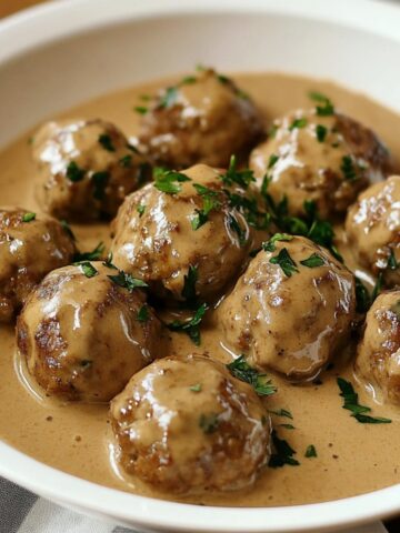 Homemade Swedish meatballs in creamy brown gravy, topped with fresh parsley, served in a white bowl.
