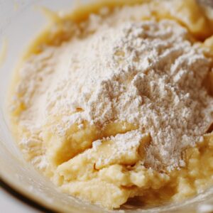 Flour sitting on top of thick banana bread batter in a mixing bowl, ready to be folded in.
