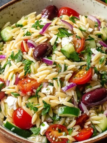 Homemade Greek orzo salad with cherry tomatoes, cucumber, red onion, Kalamata olives, feta cheese, and parsley in a rustic bowl, lightly dressed with olive oil.