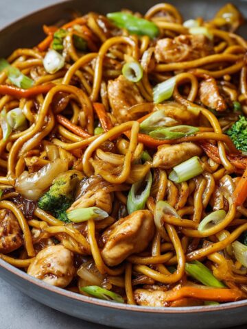 Chicken Lo Mein Recipe in a skillet with glossy noodles, tender chicken pieces, broccoli florets, carrots, onions, and scallions tossed in a rich soy-based sauce — perfectly caramelized and ready to serve, showing real home-cooked texture and freshness.