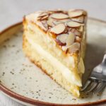 Slice of bee sting cake with creamy vanilla filling and honey-glazed almond topping on a plate.
