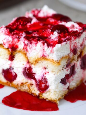 Homemade Cherry Amaretto Tiramisu with whipped cream, cherries, and cherry syrup on top, served on a white plate.
