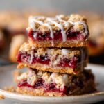 A stack of freshly baked Cherry Pie Bars with a golden, crumbly oat topping, filled with rich cherry filling and topped with a light drizzle of icing.