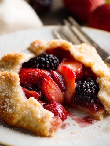 Homemade Mini Fruit Galettes blackberry galette on a white plate, showing the flaky pastry crust and thick, glossy berry filling with visible fruit slices and juices.