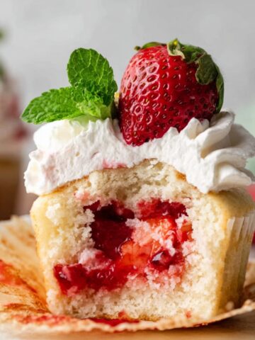 Homemade Strawberry Shortcake Cupcakes filled with strawberry compote and topped with whipped cream, strawberry, and mint