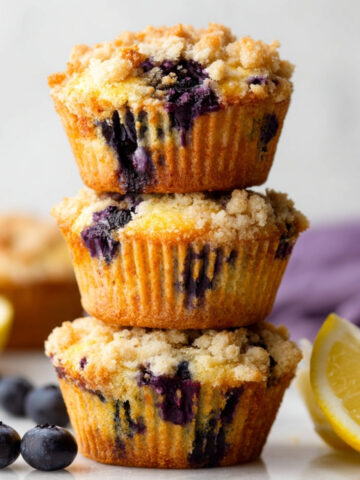 Stack of Lemon Blueberry Muffins Recipe with crumb topping, fresh blueberries and lemon on the side