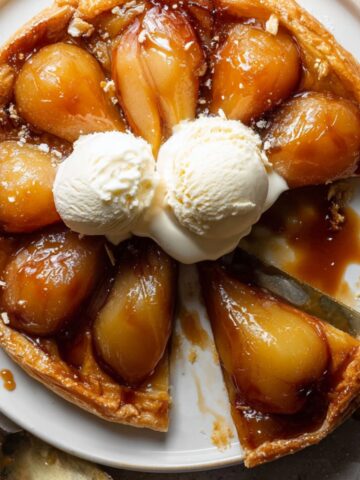 Pear Tarte Tatin Recipe with caramelized pears and flaky crust, topped with vanilla ice cream and one slice removed.