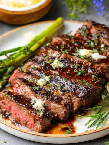 Juicy grilled Steak Marinade served with roasted asparagus, garlic, and fresh herbs, topped with melted butter for extra flavor.