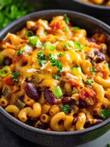 Bowl of Vegetarian Chili Mac topped with melted cheddar cheese, green onions, and parsley