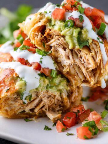 Baked Chicken Chimichangas, with shredded chicken filling and topped with sour cream, guacamole, and fresh diced tomatoes.