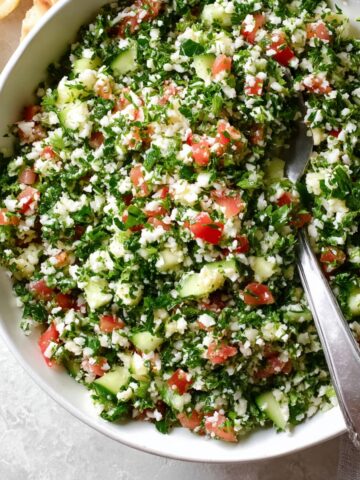 The final mixed Cauliflower Tabbouleh, with a blend of cauliflower rice, tomatoes, cucumbers, green onions, and parsley, ready to be served.