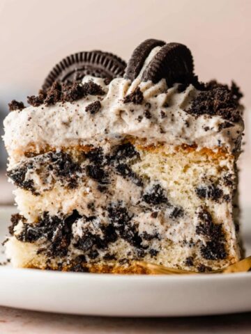 A close-up image of a slice of Cookies and Cream Cake topped with crushed Oreo cookies and creamy frosting.
