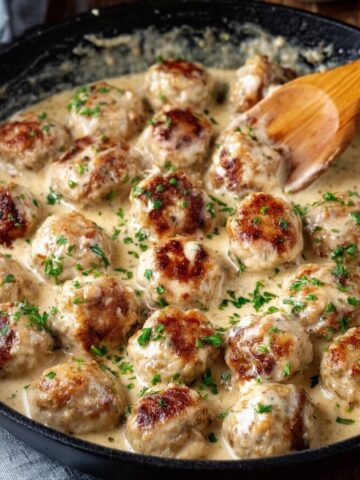 Chicken Meatballs in Cream Sauce in a pan with a wooden spoon stirring them