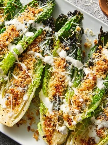 Grilled Romaine Caesar Salad lettuce topped with toasted panko breadcrumbs, grated parmesan, and Caesar dressing, offering a smoky and crunchy twist on the classic Caesar salad.
