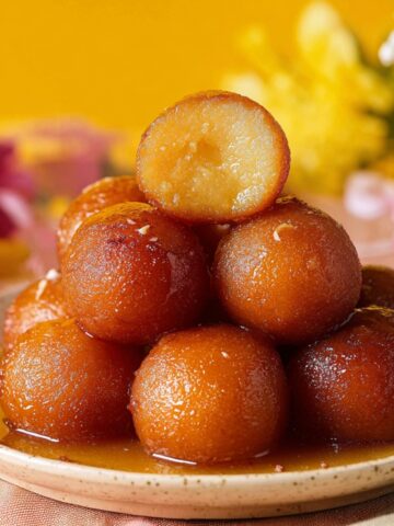 A plate of perfectly Gulab Jamun with Milk Powder soaked in sweet syrup, with one ball cut open to show its soft interior.