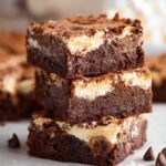 A stack of rich, fudgy marshmallow brownies with a golden, marshmallow topping, showing the smooth chocolate layers inside.