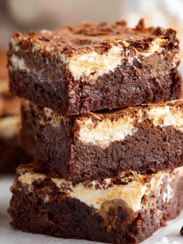 A stack of rich, fudgy marshmallow brownies with a golden, marshmallow topping, showing the smooth chocolate layers inside.