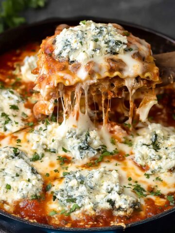 A hearty serving of Mushroom alla Vodka Stovetop Lasagna with melted cheese and spinach filling, served with a wooden spatula lifting a cheesy layer.