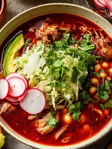 Bowl of Pork Pozole Rojo topped with cabbage, radishes, cilantro, avocado, and hominy in rich red broth.