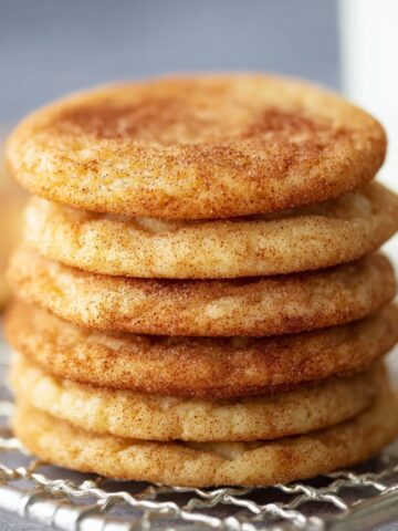 Freshly baked Snickerdoodle Cookies stacked on a wire rack with a glass of milk.