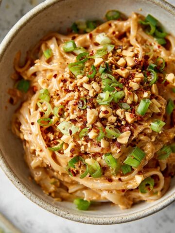 A bowl of Spicy Peanut Butter Noodles topped with green onions, crushed peanuts, and red chili flakes, creating a vibrant and flavorful dish.