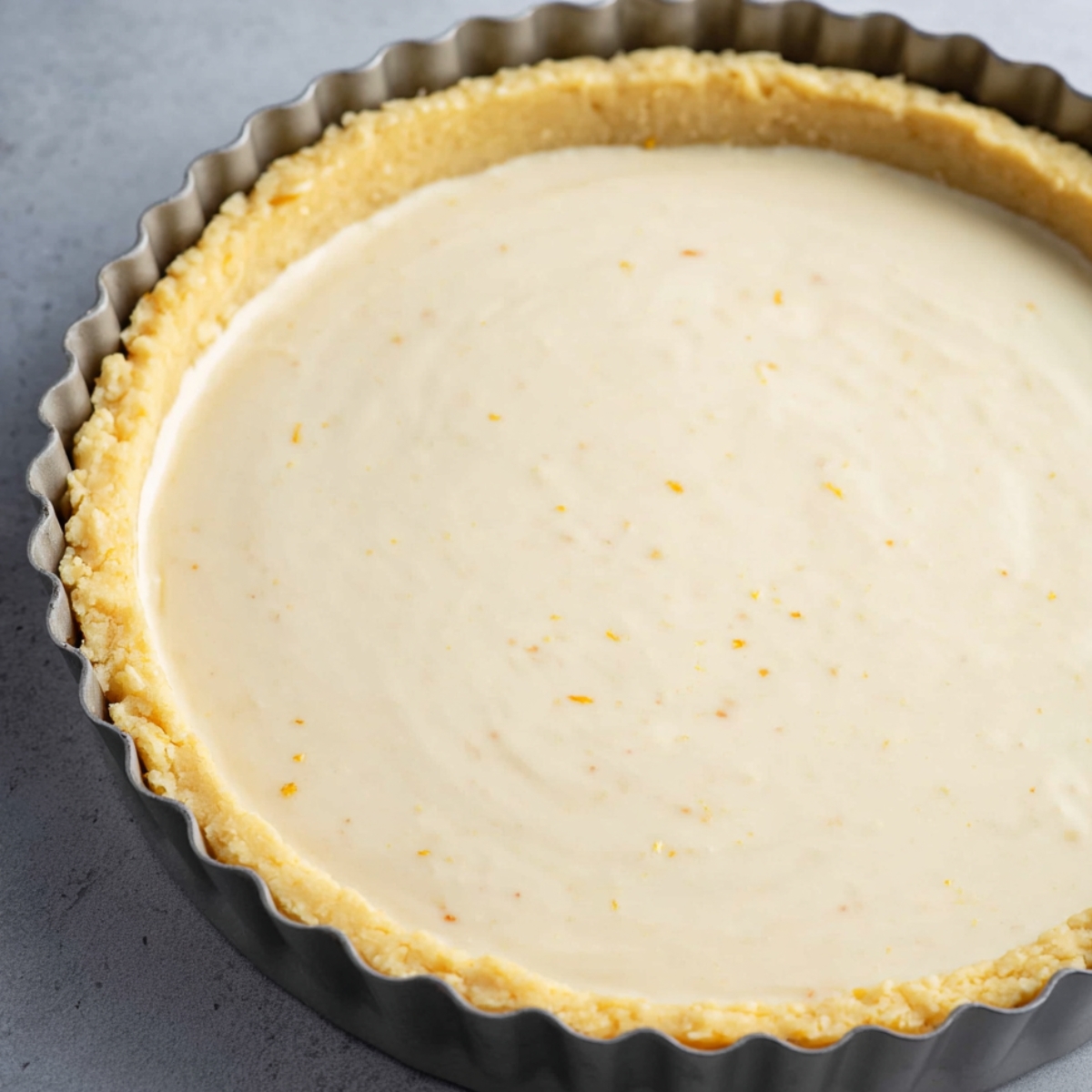 Close-up image of a pie crust filled with smooth custard filling, ready for baking. The top of the filling is even, with a hint of lemon zest visible.