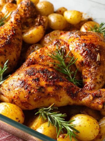 Baked Chicken Leg Quarters surrounded by roasted baby potatoes and fresh rosemary sprigs, showing a deliciously seasoned dish.