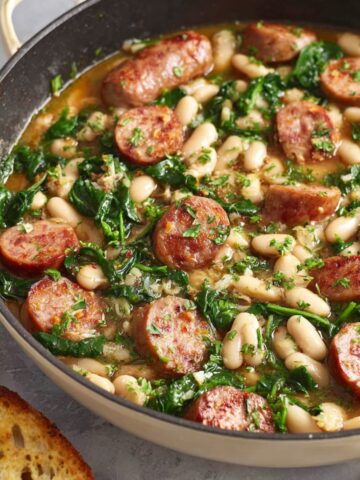 A hearty Chicken Sausage White Bean Skillet, with fresh spinach, beans, and sausage slices cooked together in a savory broth, garnished with parsley.