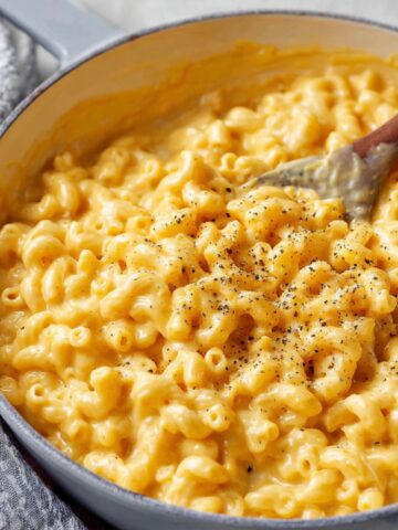 Creamy Homemade Mac and Cheese in a pot with a wooden spoon stirring, made with elbow macaroni and cheddar cheese sauce.