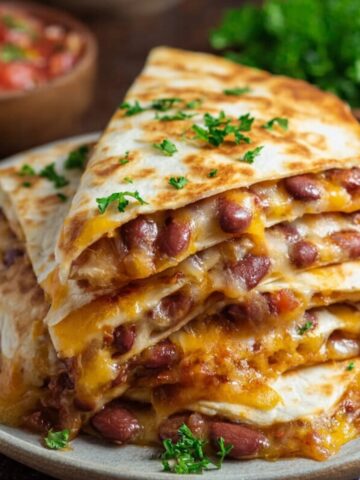A close-up of Kidney Bean Quesadillas, melted cheese, and garnished with parsley on a brown plate.