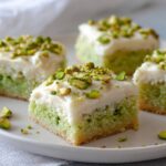 A close-up of Pistachio Cookie Bars topped with cream cheese frosting and chopped pistachios on a plate.